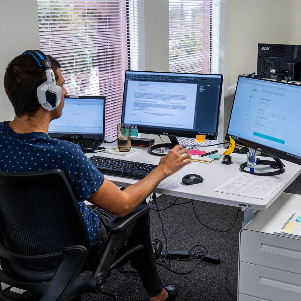 A registered agent working at a desk with a laptop and two monitors.