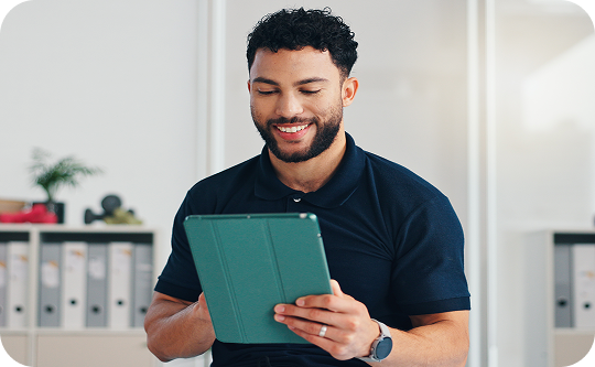 Man smiling and looking down at a tablet he is using.