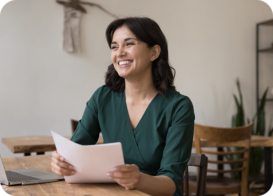 Woman sitting in front of a laptop smiling and holding a stack of papers.