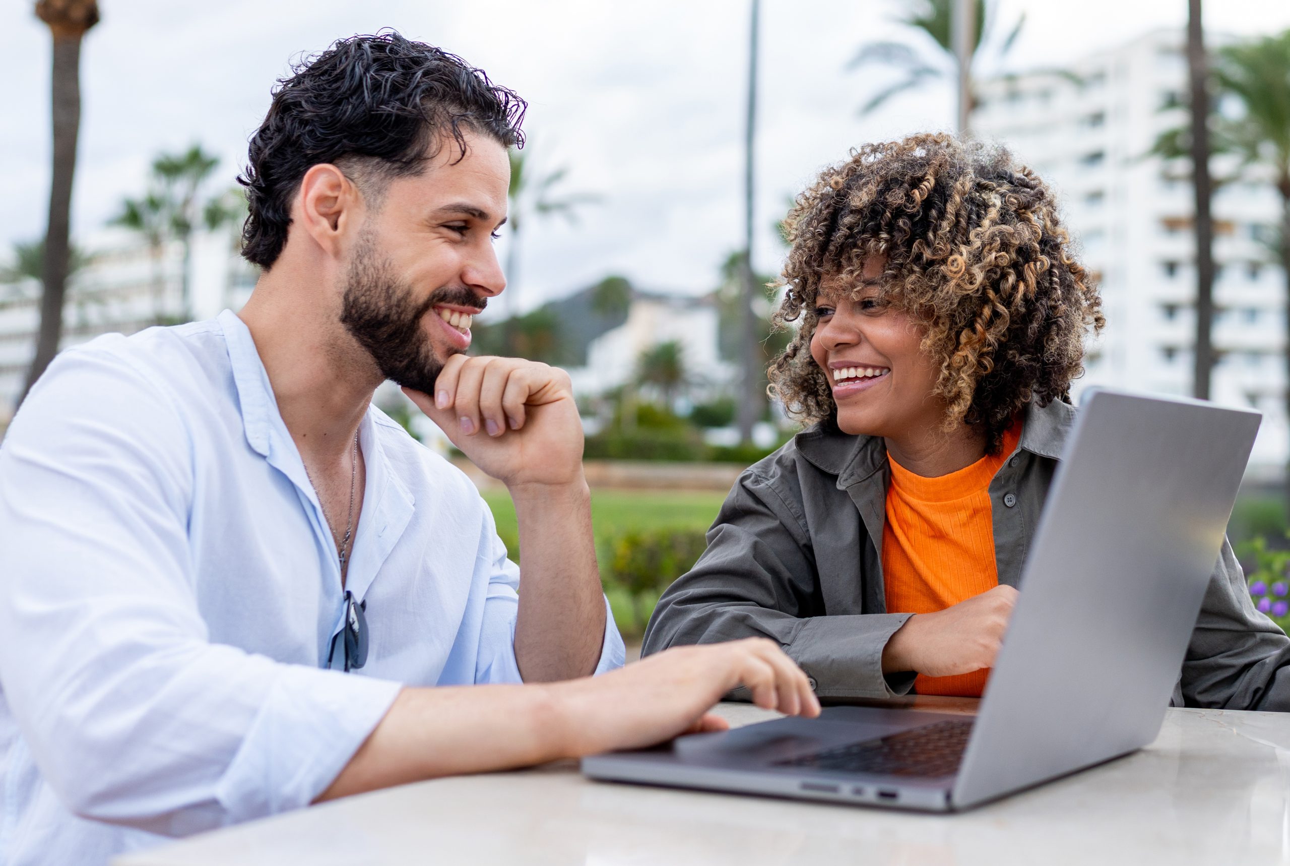Two people smiling while checking information a laptop at an outdoor meeting.