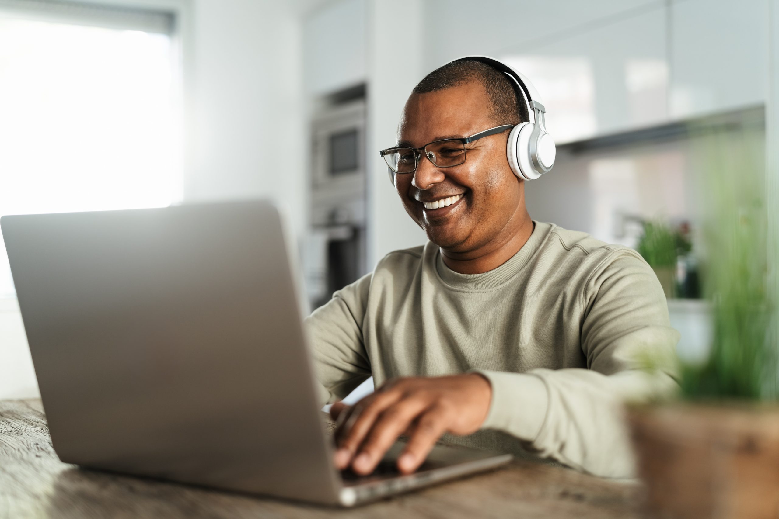 Man with headphones, smiling while typing on a laptop